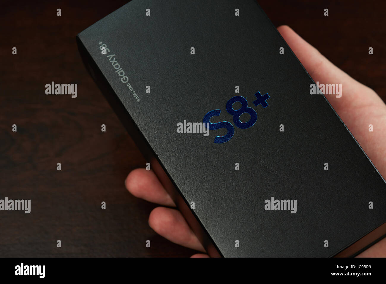 New York, USA - 12. Juni 2017: Hand halten Feld der neuen Samsung s8 plus auf dunklem Braun aus Holz Stockfoto