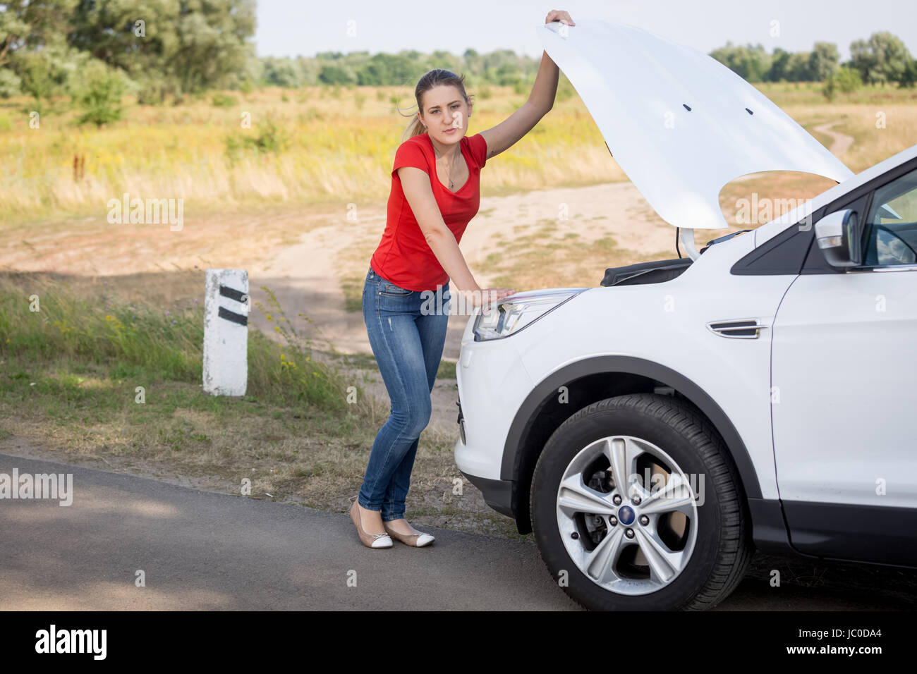 Junge Frau Öffnung Haube von dem kaputten Auto am Straßenrand Stockfoto