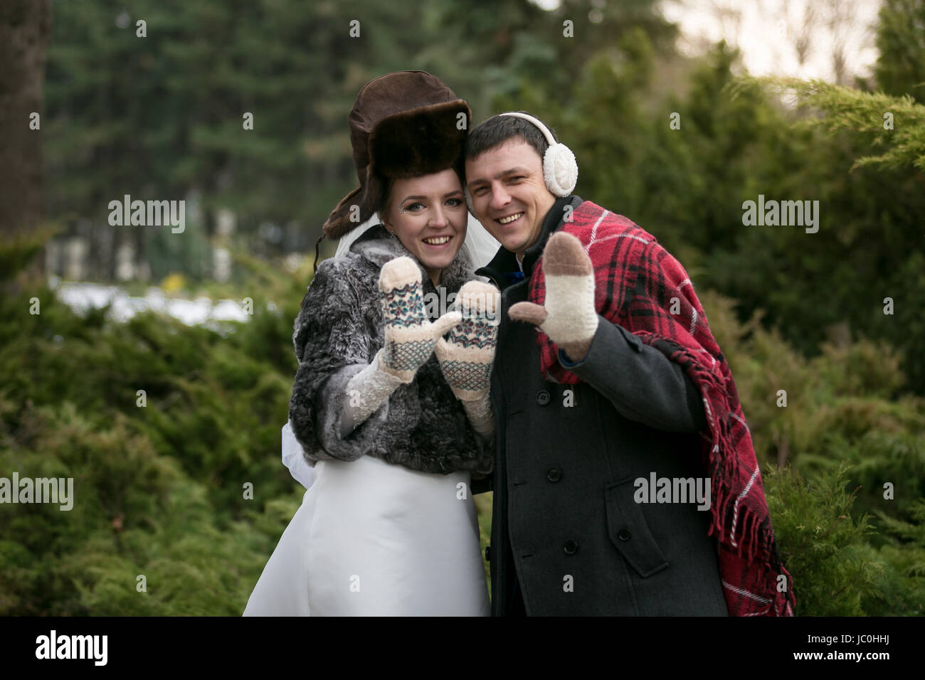 Lustige Porträt des frisch verheirateten Paares in Schals und Mützen posiert im Winterwald Stockfoto