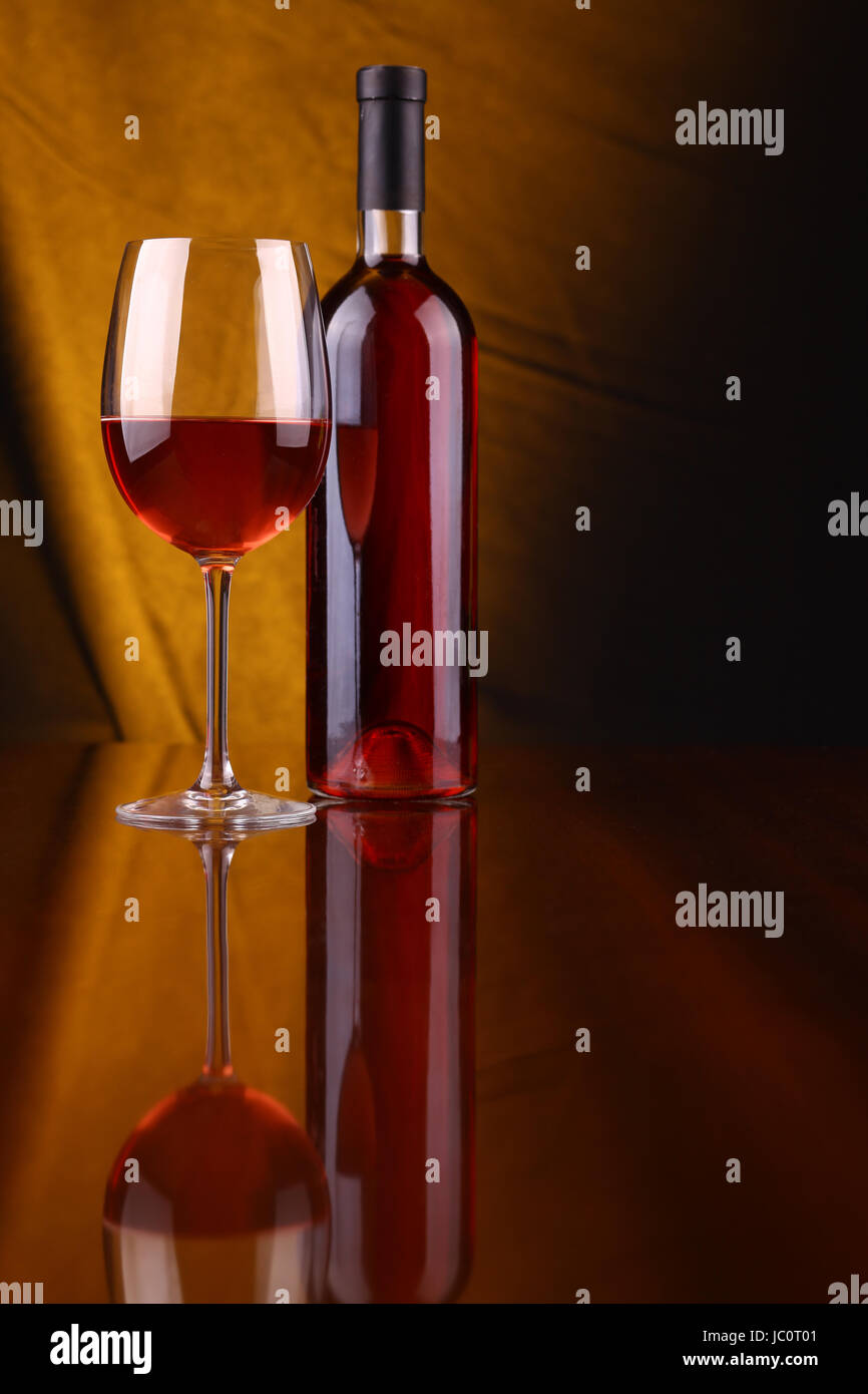 Glas und Flasche Roséwein über einem drapiert Hintergrund leuchtet gelb Stockfoto