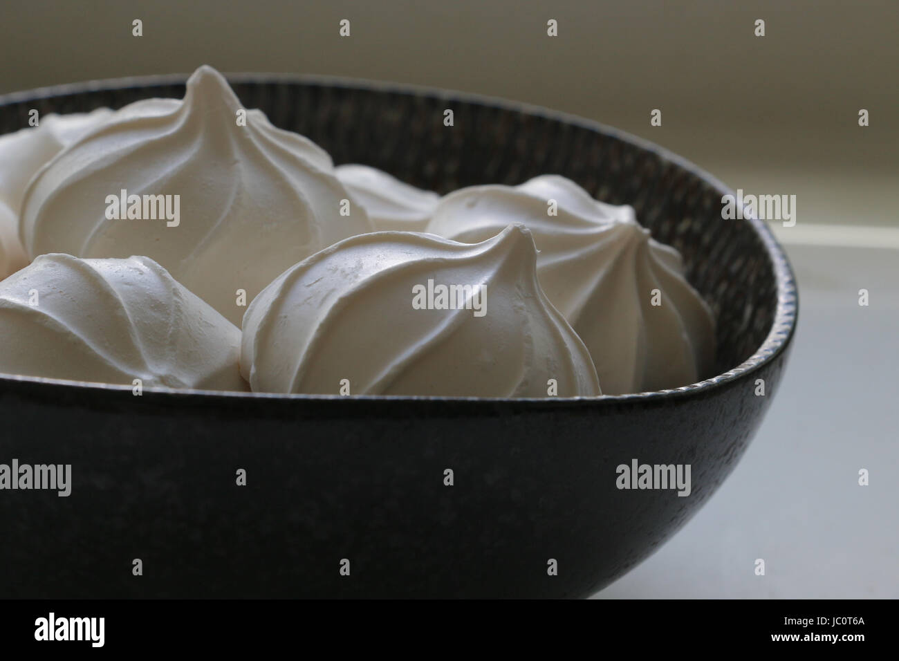 Schwarze Schale gefüllt mit weißen Baiser Cookies, im Profil unter natürlichem Licht gesehen. Stockfoto