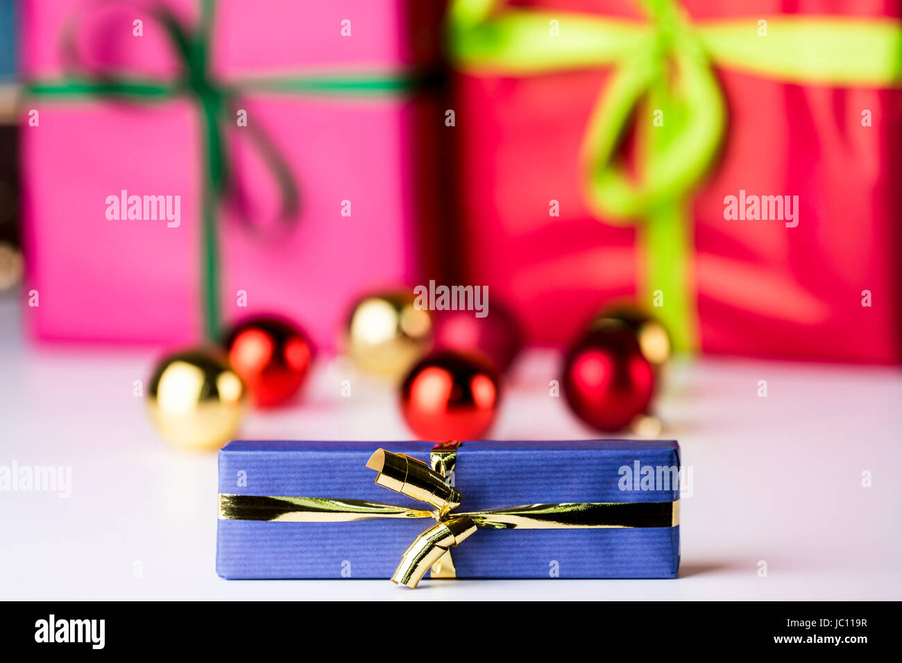 Glitzer Kugeln und Bowknots in soft-Fokus bringen die scharfen Konturen der blauen eingewickelt Gegenwart mit der goldenen Schleife vorne. Stockfoto
