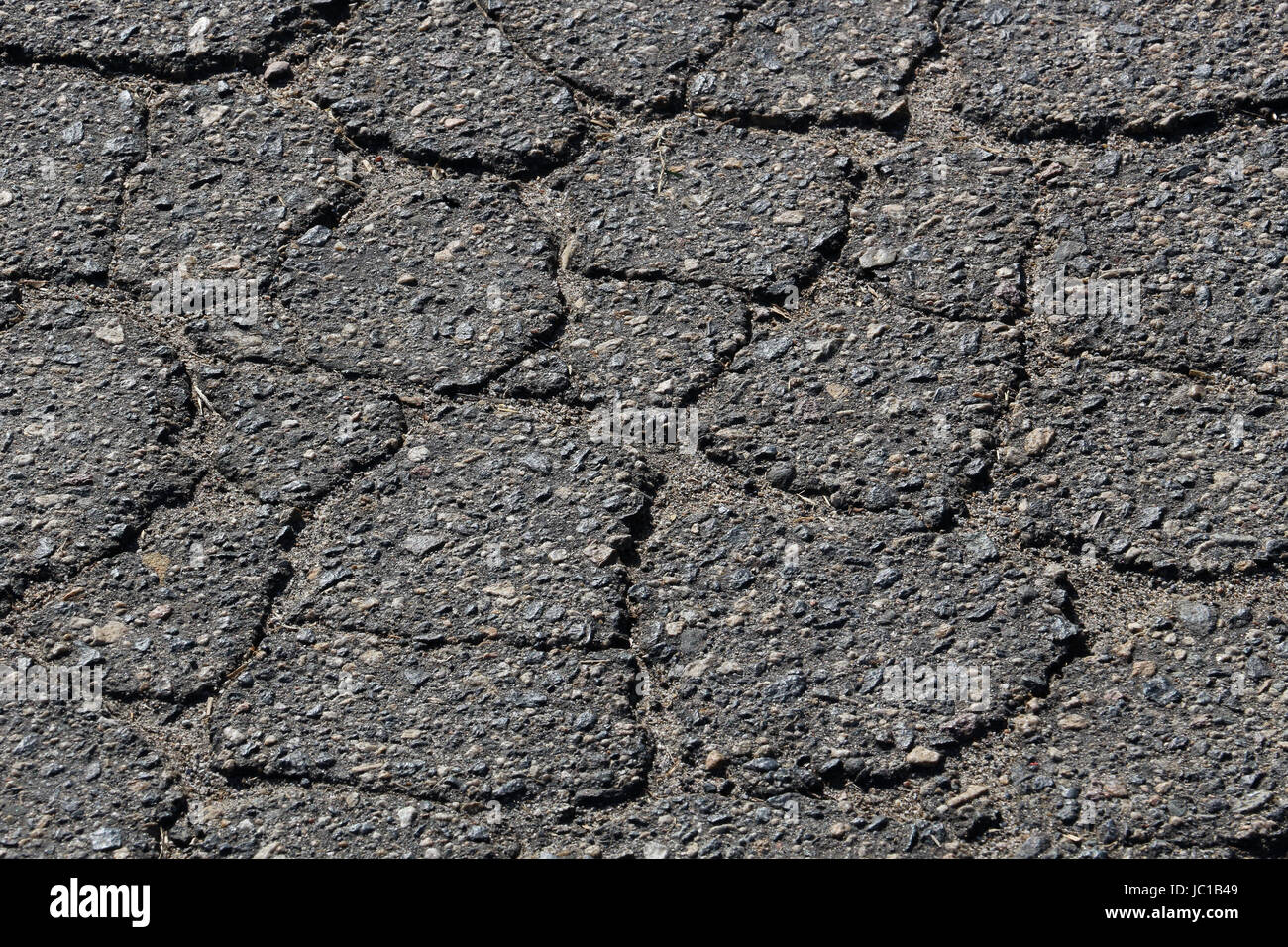 Bröckelt schwarzer Asphalt Gleisbett, Rissbildung in einem netzförmigen Muster, mit Flecken von Kies. Schlecht gewartete Asphaltstraße.  Braucht Pflege. Stockfoto
