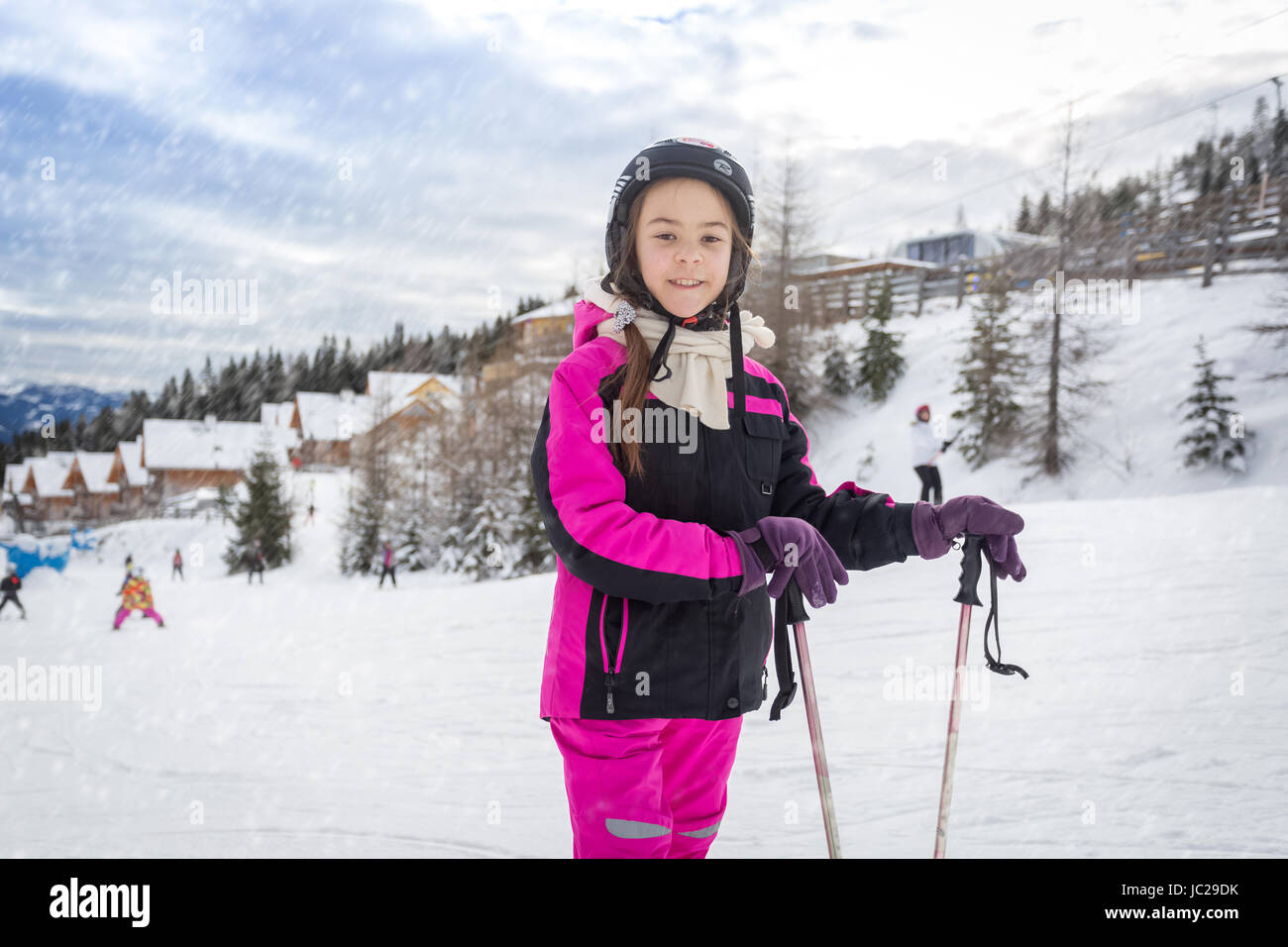 Schönes Lächeln auf den Lippen Mädchen im Skianzug posiert mit Skistöcken am Hang Stockfoto