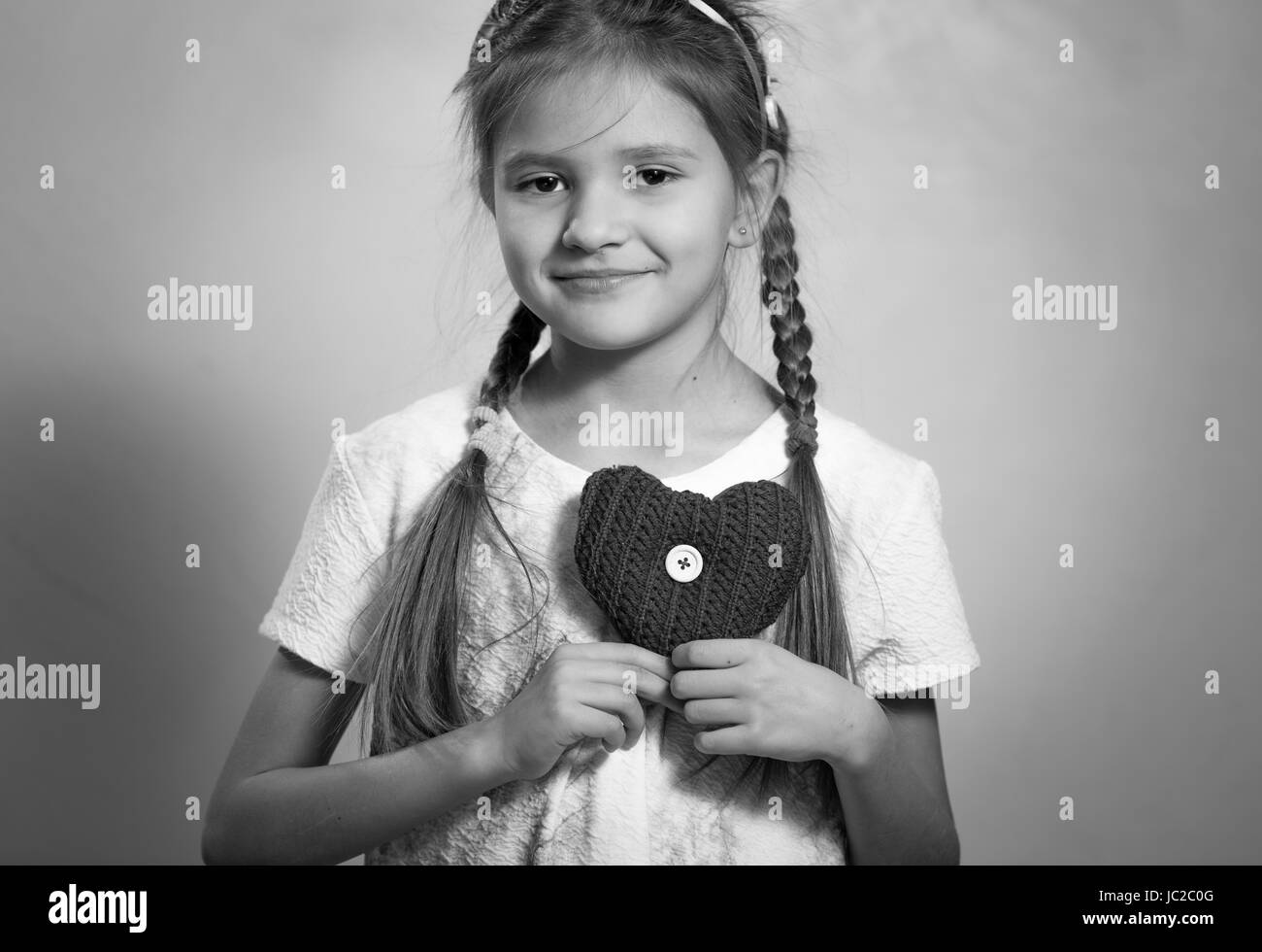 Monochrome Portrait von niedlichen lächelndes Mädchen hält dekorative Herz auf Brust Stockfoto