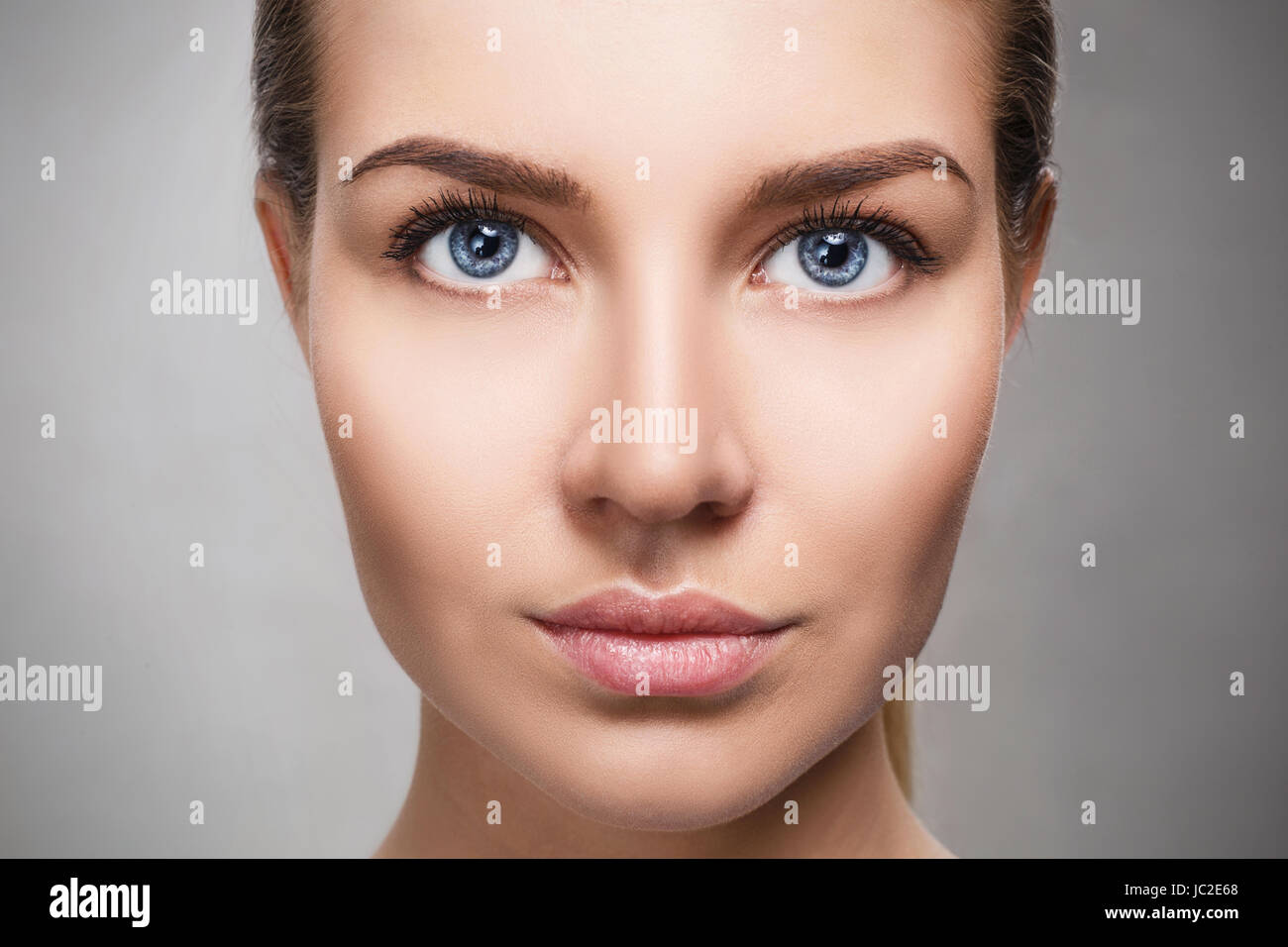 Schönes Gesicht der jungen Frau mit perfekter Haut und Make-up. Frische Haut Nahaufnahme auf grauem Hintergrund. Beauty Portrait. Stockfoto