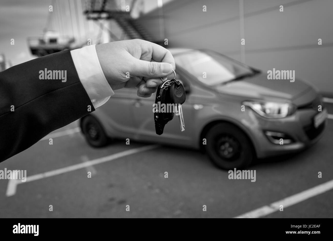 Closeup schwarz-weiß Foto der Mann im Anzug mit Autoschlüssel gegen Neuwagen Stockfoto