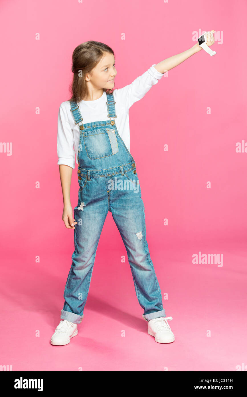 Entzückende kleine Mädchen in Denim-Overalls Smartwatch halten und Lächeln Stockfoto