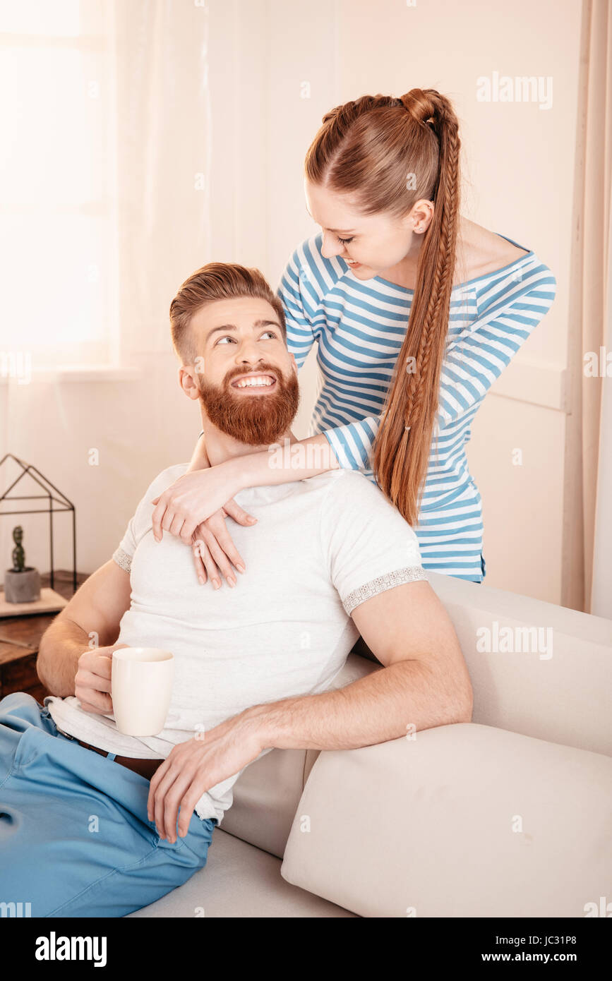 Schöne junge Frau umarmt schön bärtigen Mann sitzt zu Hause auf sofa Stockfoto