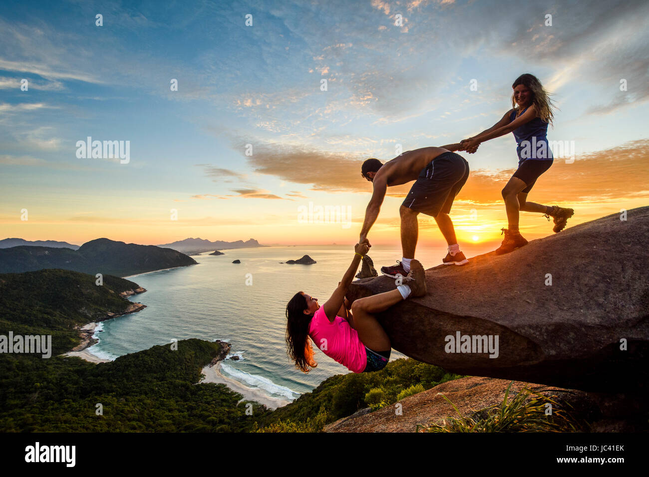 Zwei Personen hilft Frau bei Sonnenuntergang Felsen erklimmen, Pedra Telegrafo, Rio De Janeiro, Brasilien Stockfoto