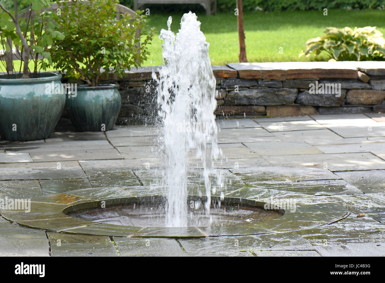 Eine formale Wasserfontäne spritzt auf einer steinernen Terrasse. Stockfoto