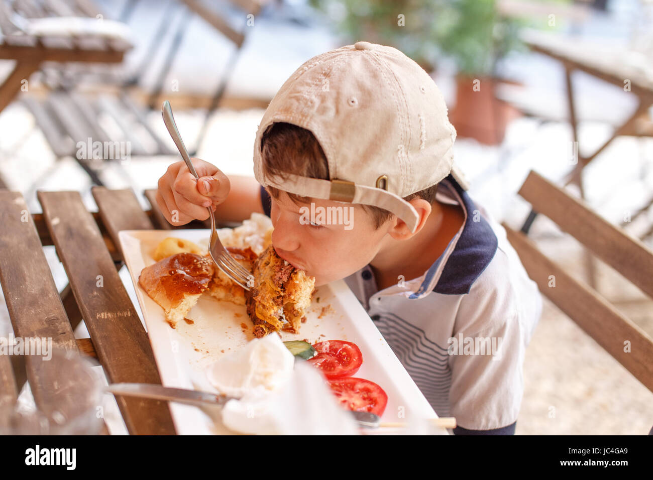 Kleine böse Junge Essen Junk Food im Restaurant unter freiem Himmel Stockfoto