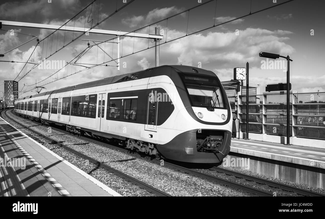 Elektrischer Zug geht in der Nähe von Bahnsteig in Amsterdam, Niederlande. Schwarz / weiß Foto Stockfoto