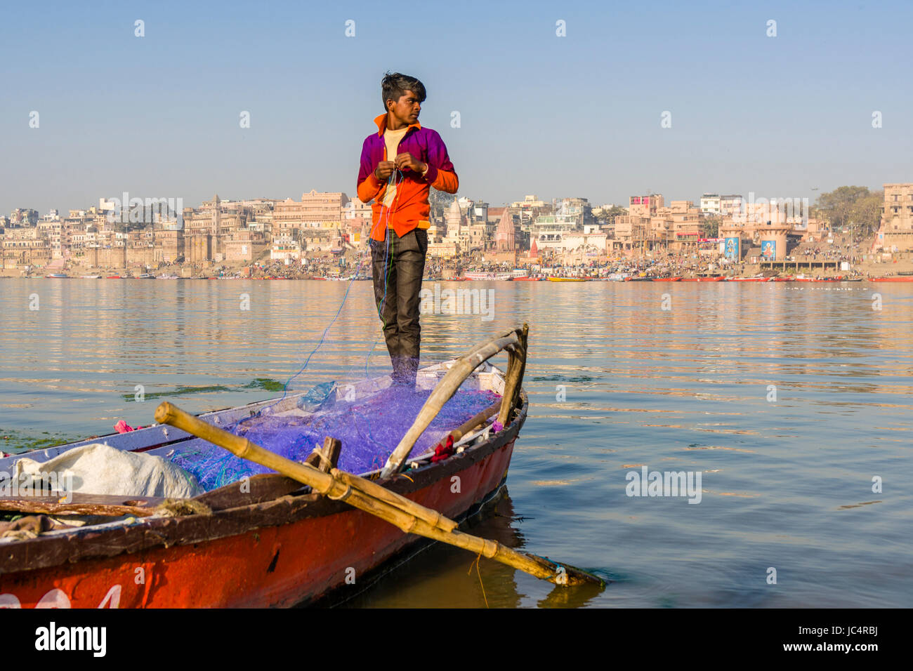 Ein Fischer ist die Reparatur eines Net auf den Sandbänken am heiligen Fluss Ganges, Panorama der dashashwamedh Ghat, main Ghat, in der Ferne Stockfoto