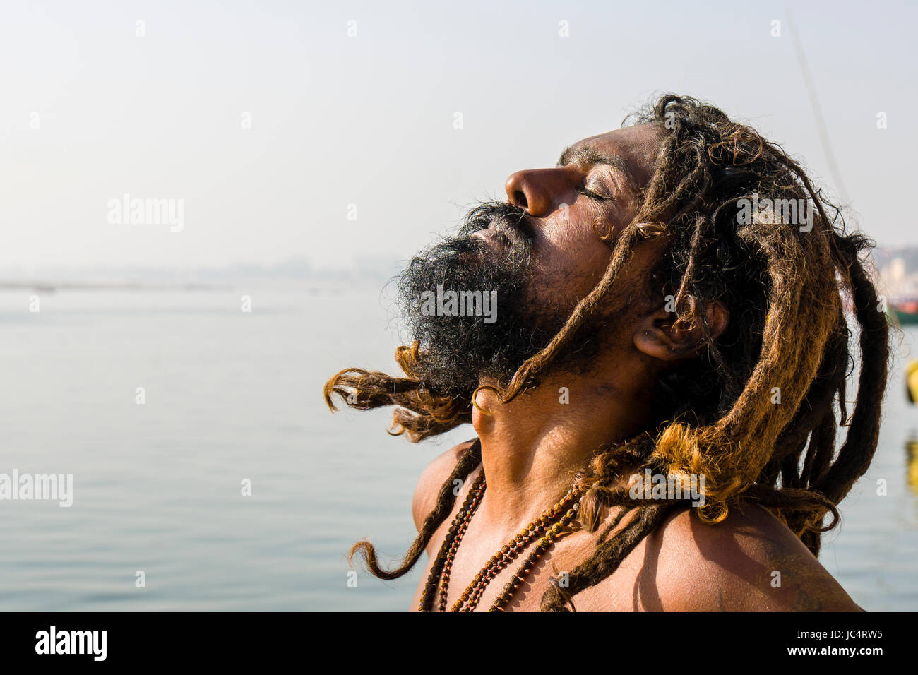 Ein Sadhu, Heiliger Mann, sitzt und Beten auf einer Plattform am heiligen Fluss Ganges Meer Ghat im Vorort Godowlia Stockfoto