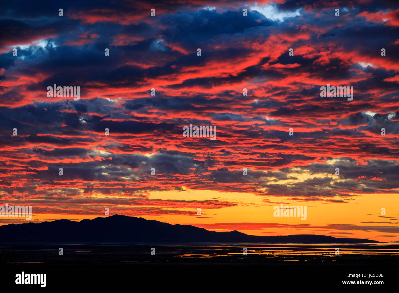 Das Abendrot des Sonnenuntergangs leuchtet auf der Unterseite der Wolken über Antelope Island.  Antelope Island ist die größte Insel im Great Salt Lake. Stockfoto