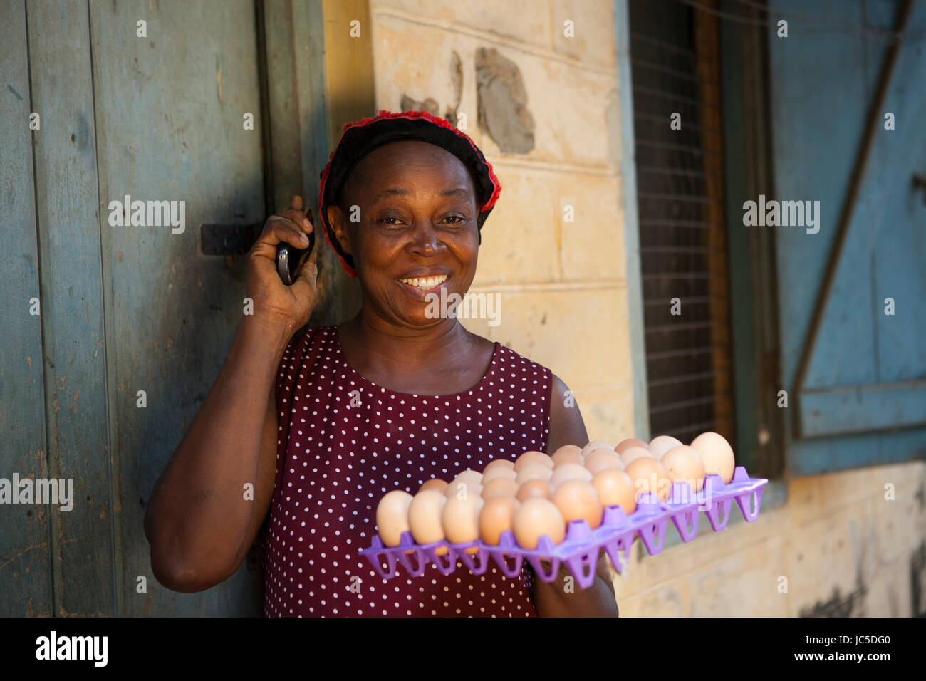 Eine weibliche Geflügel Landwirt mit einer Schale mit frischen Eiern, auf ihr Mobiltelefon, Nigeria, Afrika Stockfoto