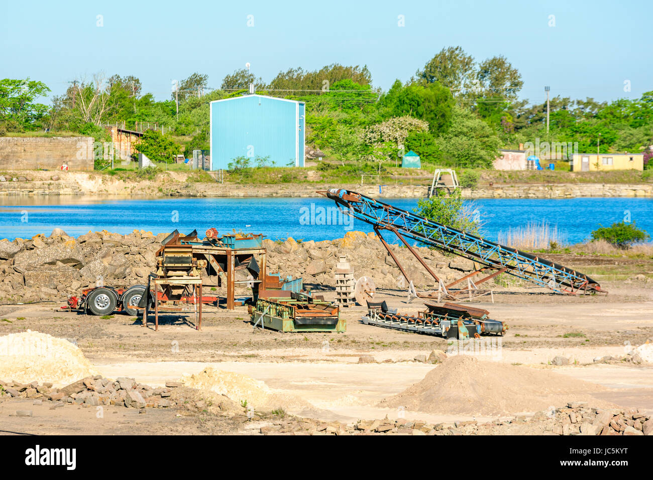 Sammlung von gebrauchten Maschinen in einem Kalksteinbruch mit Wasser gefüllte Grube im Hintergrund. Stockfoto