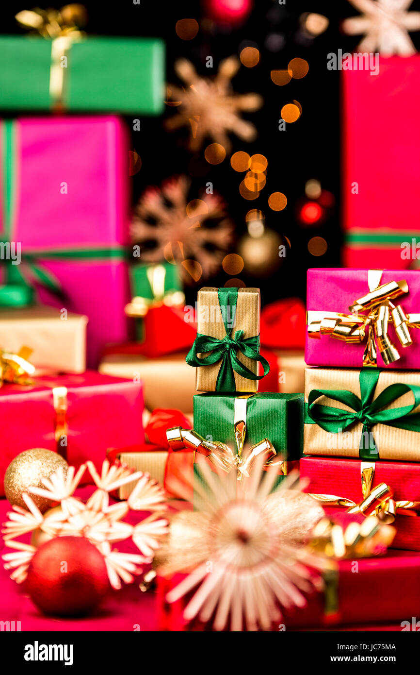 Kleine, einfarbige Weihnachtsgeschenke stapelten sich zwischen den Sternen und Kugeln. Engen Schärfentiefe. Konzentrieren Sie sich auf kleine goldene Box mit grünen Bogen. Out-of-Focus Lichtpunkte auf schwarzem Hintergrund. Stockfoto