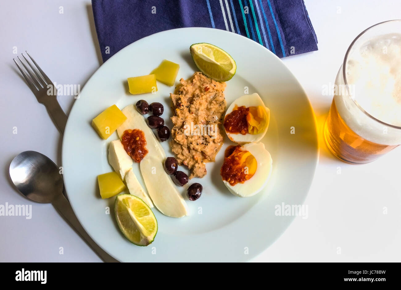 Eine kalte Mahlzeit für den Sommer: Würziger Thunfisch-Salat, hartgekochtes Ei, Mozzarella, Cheddar-Käse, Oliven, mit heißer Sauce, Limette und Bier Stockfoto