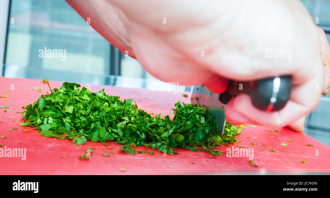 Männlichen Chef schneiden Petersilie mit großen Messer auf Schneidebrett rot Stockfoto