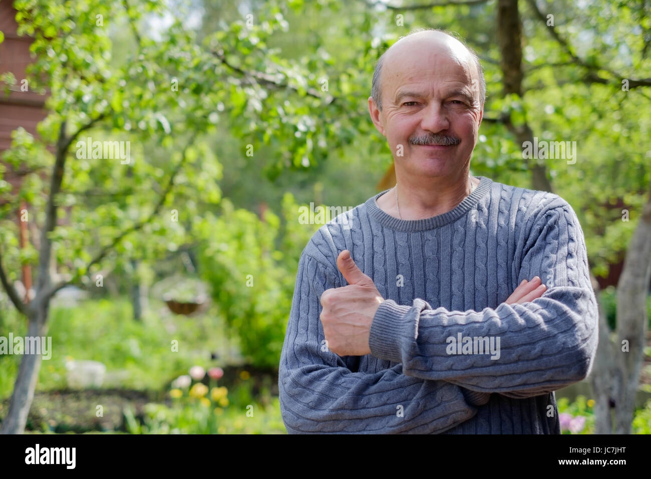 Reifer Mann sitzen im Garten in der Nähe von Apfelbaum im Lande. Er zeigt thump up. Stockfoto