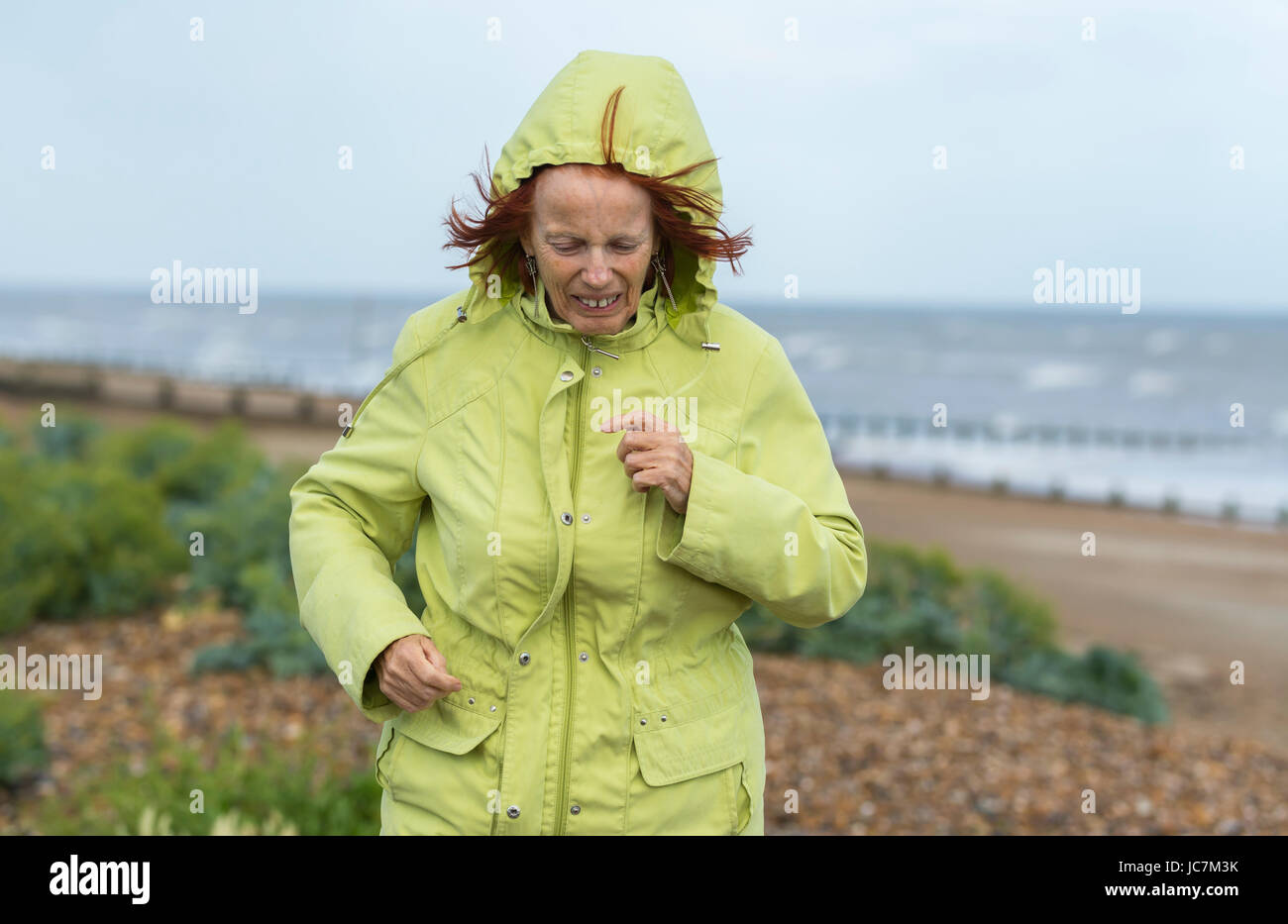 Frau mittleren Alters, die auf einem Strand in kaltem Wetter in einem Mantel bekleidet warm zu halten, an trüben Tagen in Großbritannien. Stockfoto