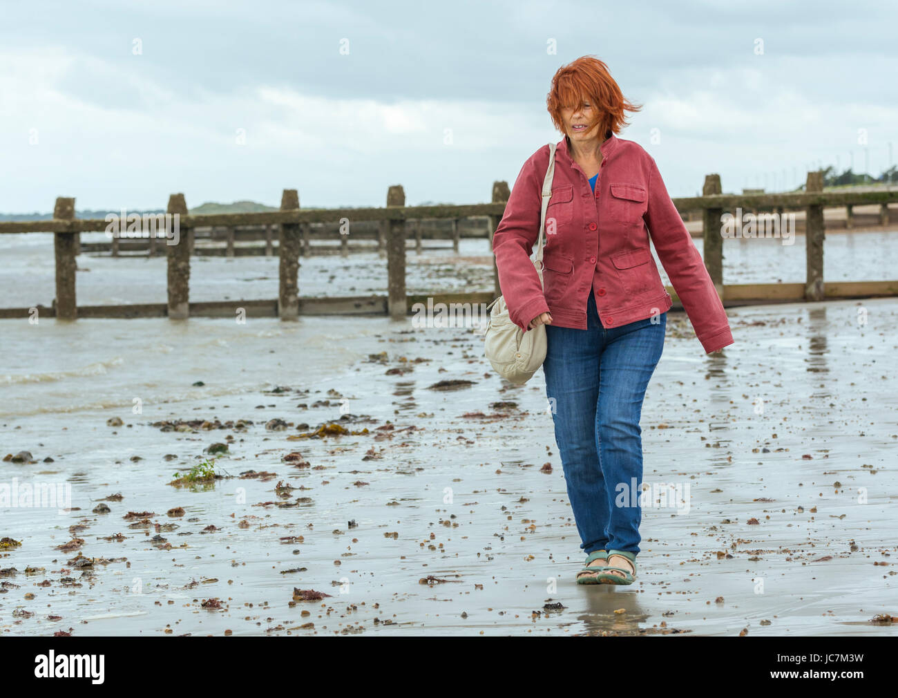 Ältere aber jünger aussehende Frau zu Fuß am Strand bei Ebbe, aktiv zu bleiben. Senior aktiv bleiben. Stockfoto