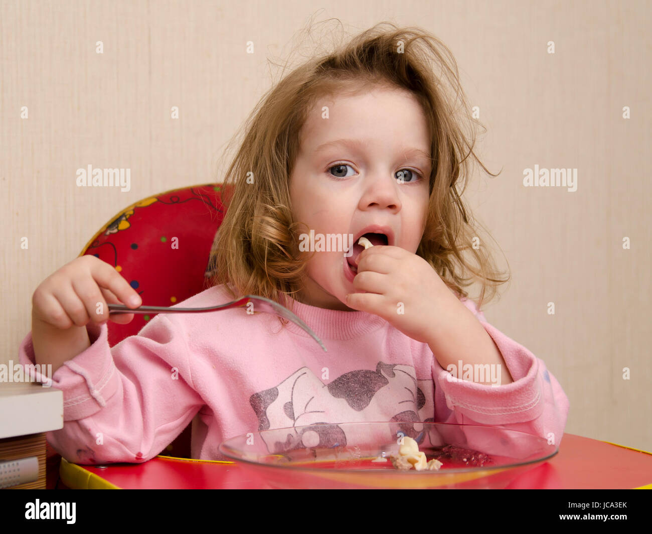 Zwei-jährigen Mädchen isst sitzen am Tisch in der Küche. Mädchen isst mit einer Gabel einstechen. Stockfoto