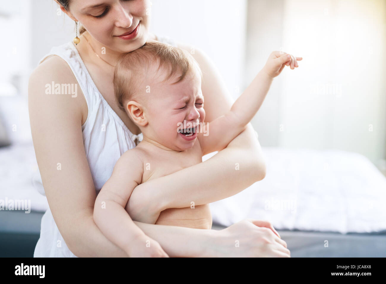 Junge Frau mit schreienden Baby auf Händen. Helle weiße Farben. Stockfoto