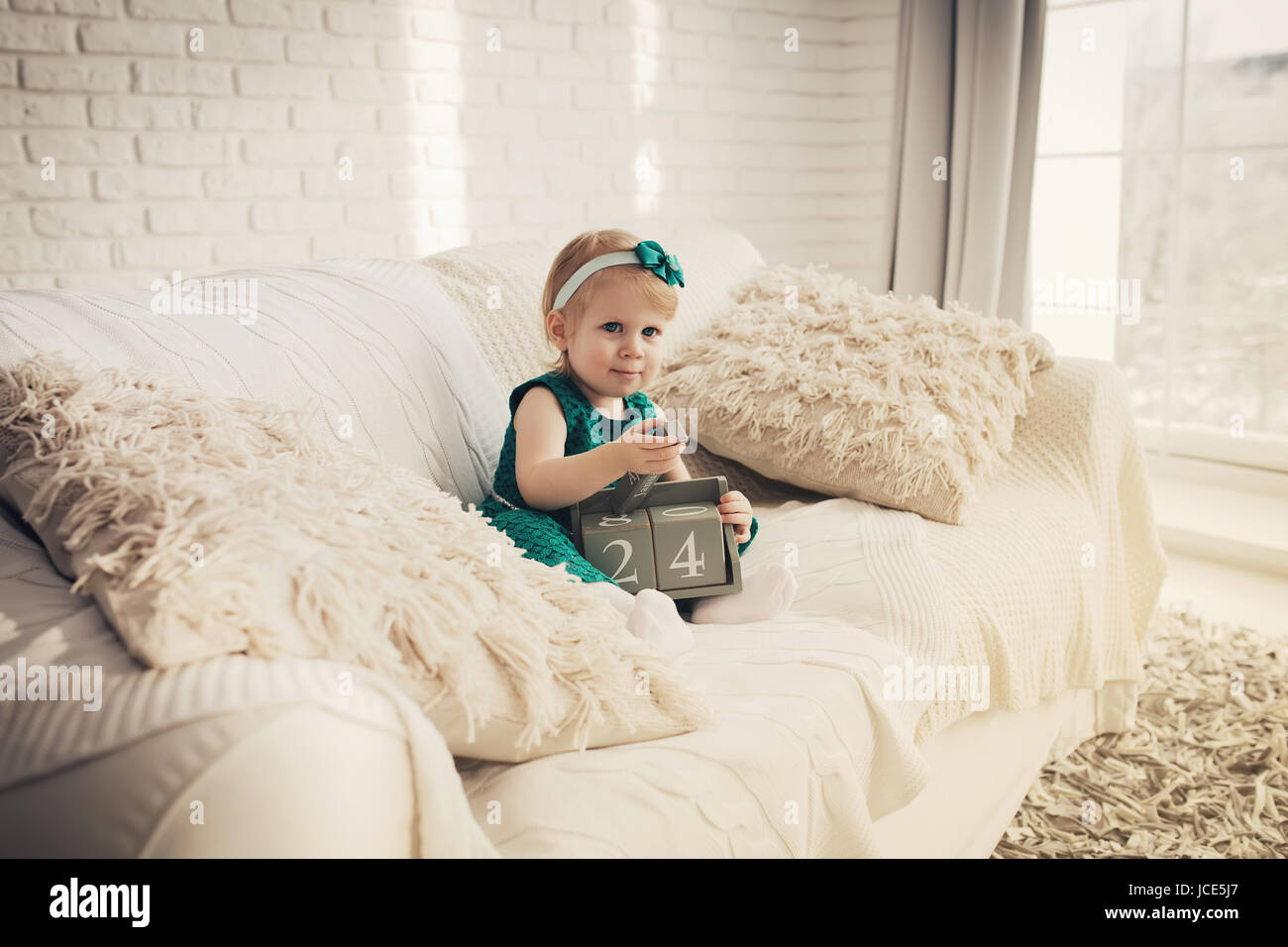 Hübsches Kind spielt auf weißen Sofa im Innenbereich. Schöne kleine Mädchen in weißen moderne Wohnung. Stockfoto
