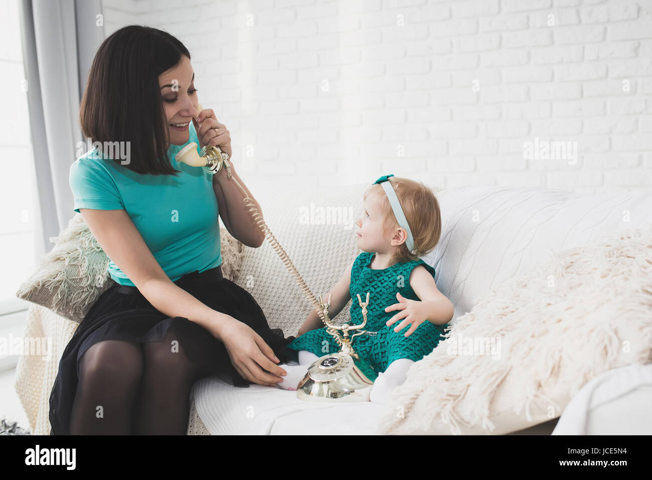 Kind und Mama spielt mit Retro-Telefon im Haus. Glückliches Mädchen und Mutter in weißen Stil Wohnung auf Sofa. Studio-Fotografie. Stockfoto