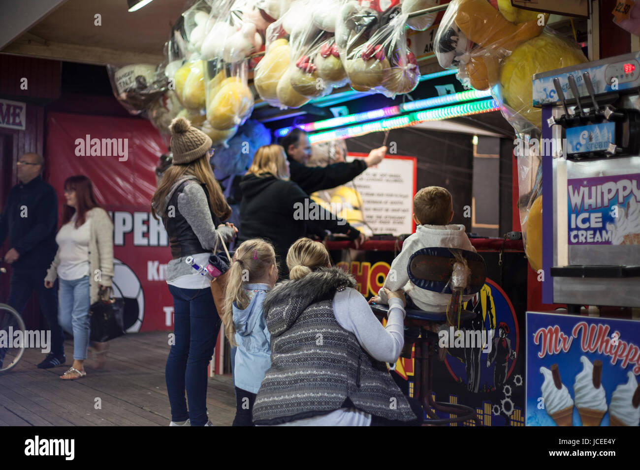 Kirmes, Fahrten und Vergnügungsparks. Menschen, die ein preisgekröntes Spiel spielen, Kinder beobachten Stockfoto