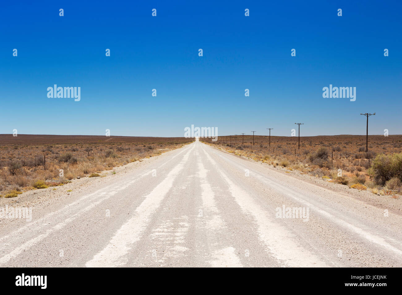 Ein gerader Feldweg durch die trockene Halbwüste der Karoo in Südafrika. Stockfoto