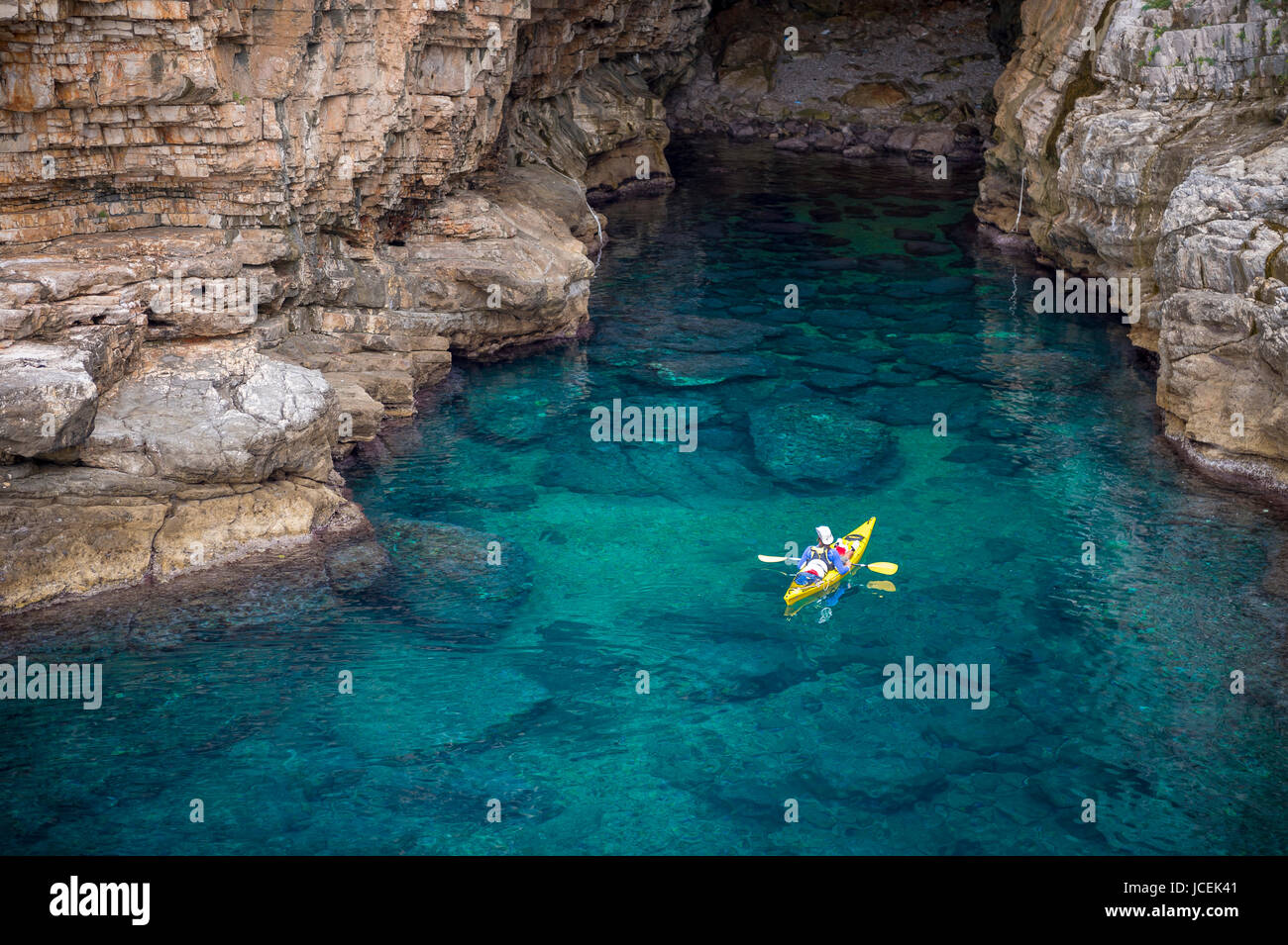 Blick von den Felsklippen der Kajakfahrer erkunden das kristallklare Wasser des Mittelmeers eine Bucht vor der Küste von Dubrovnik, Kroatien Stockfoto