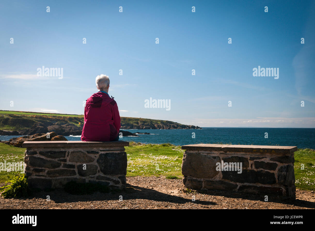 Dame trug eine rote Jacke mit Blick auf das Meer bei Portsoy, Banff & Buchan, Aberdeenshire, Schottland Stockfoto