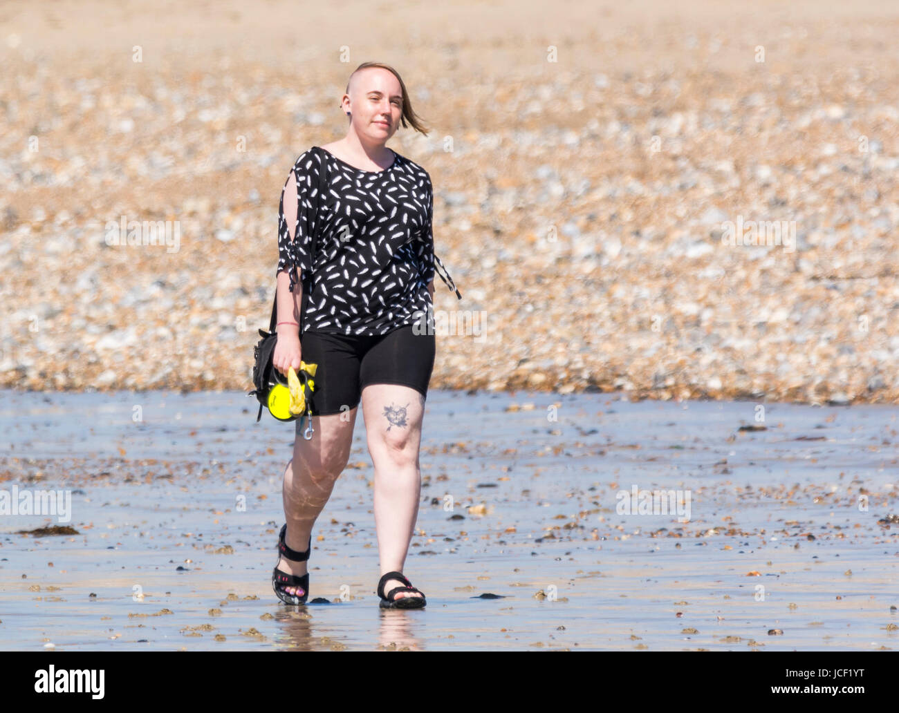 Moderne, junge Frau mit einzigartigen, modernen Frisur zu Fuß am Strand an einem heißen Tag im Sommer in Großbritannien. Stockfoto