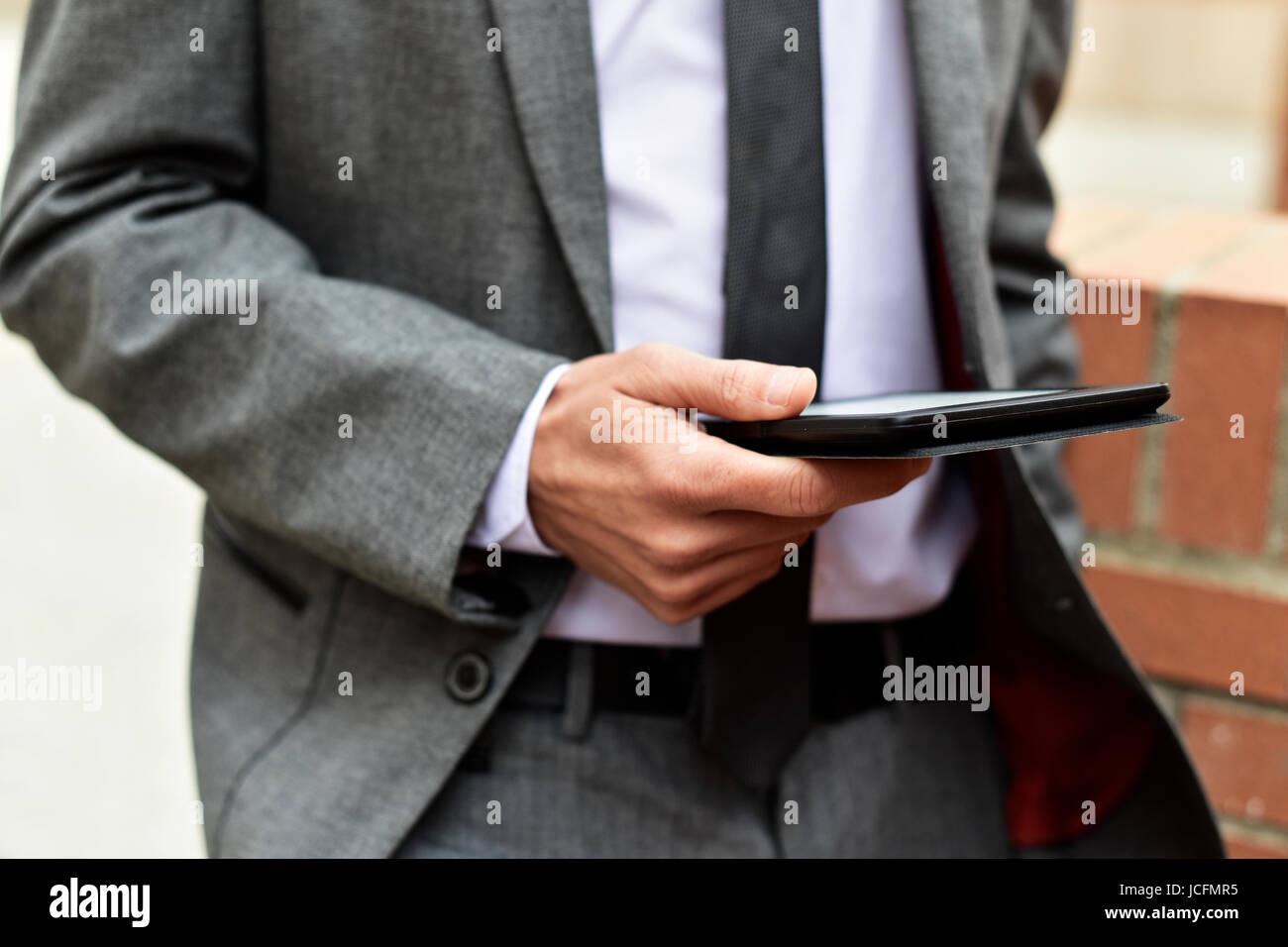 Nahaufnahme eines jungen kaukasischen Geschäftsmann in einem grauen Anzug mit einem Tablet im freien Stockfoto
