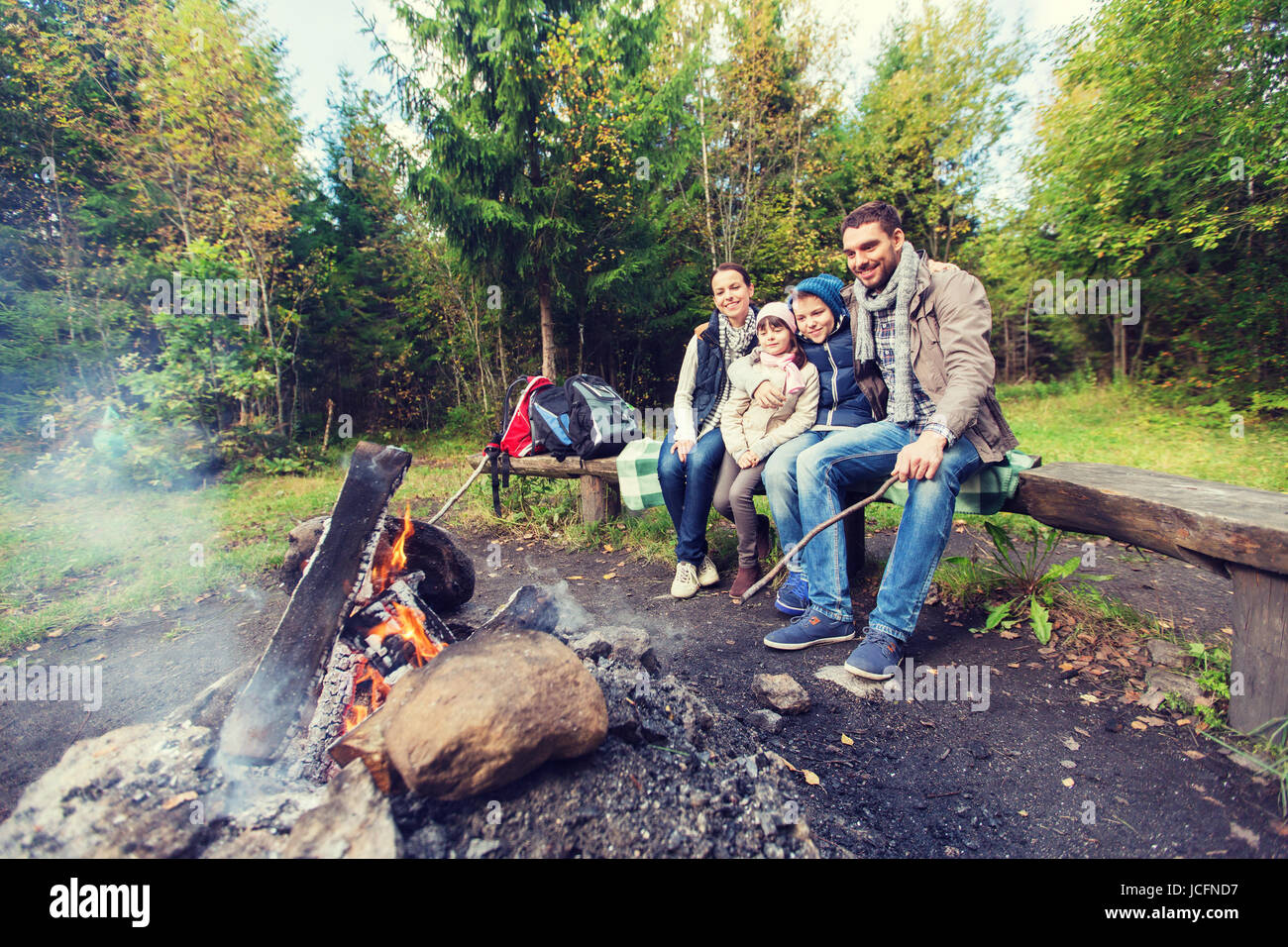 Glückliche Familie sitzt auf der Bank am Lagerfeuer. Stockfoto