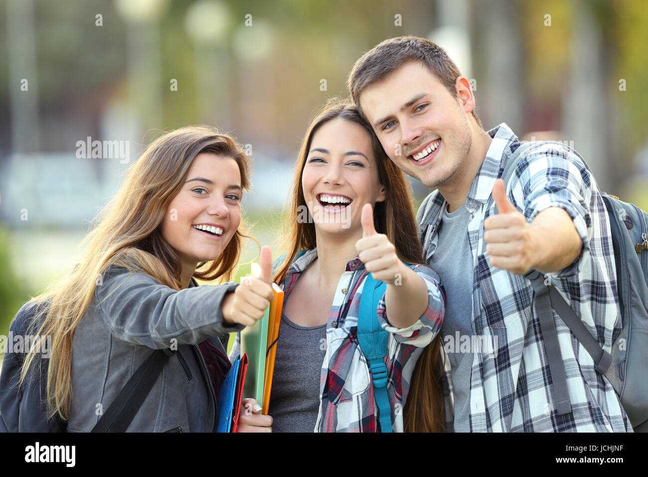 Drei glückliche Schüler betrachten Sie mit Daumen oben in einem Uni-campus Stockfoto