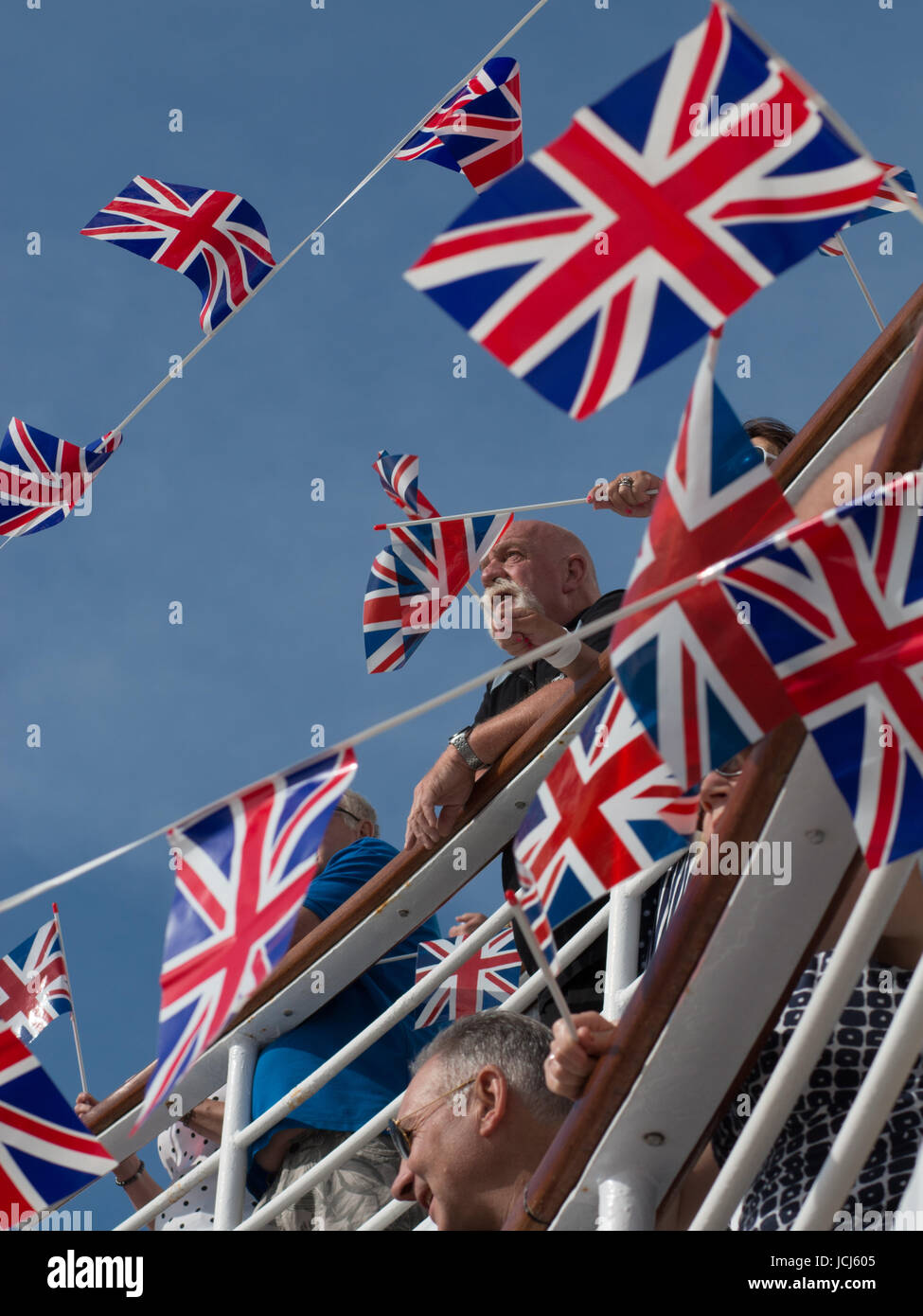 Die Kreuzfahrtpassagiere, die in einem sailaway Partei durch Union Jack Flaggen umgeben. einige Fahnen werden geschwenkt wird. Es ist ein strahlend blauer Himmel. Stockfoto