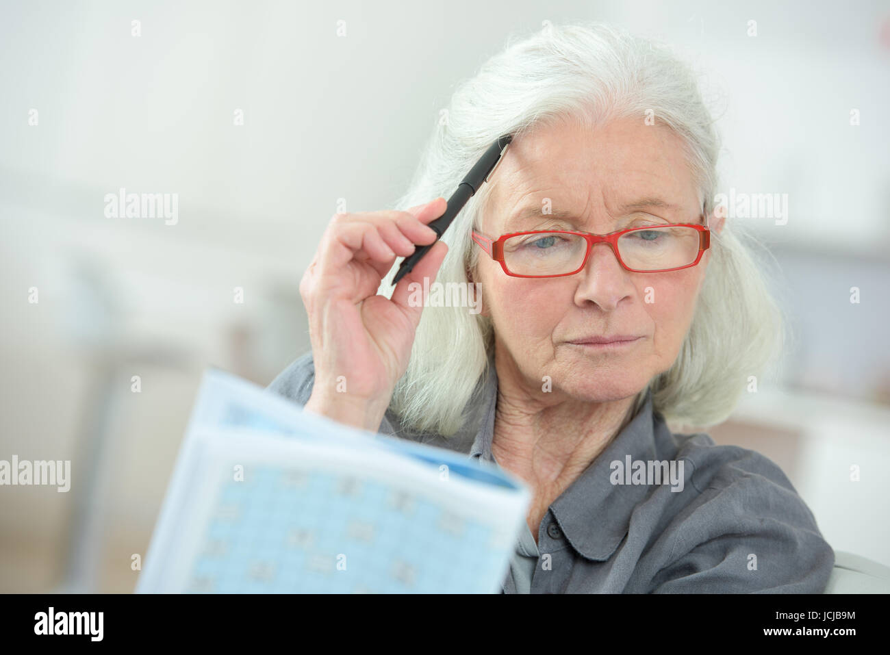 ältere Frau sitzt an einem Tisch ein Kreuzworträtsel ausfüllen Stockfoto