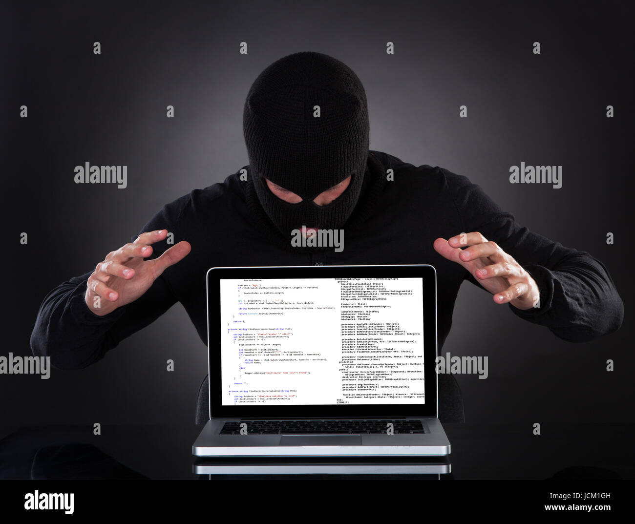 Hacker im Sturmhaube stehen in der Dunkelheit heimlich Daten aus einem Laptop-Computer zu stehlen oder das Einfügen von Spyware in einem Online-Sicherheit und Risiko-Konzept Stockfoto