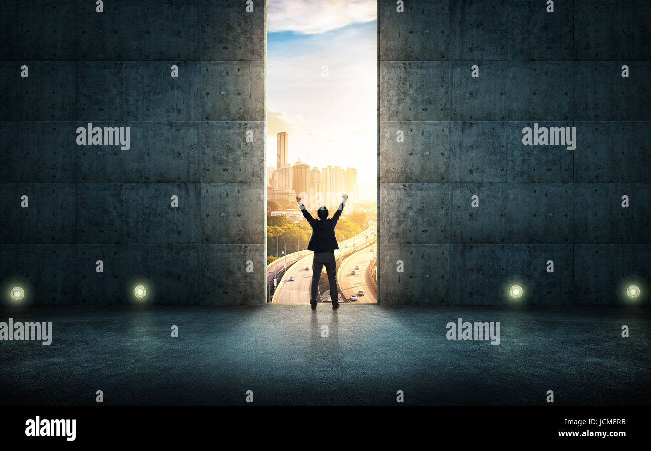 Erfolg Geschäftsmann jubeln gegen Betonwand mit großer Tür, Sonnenaufgang Szene Skyline im freien Blick auf die Stadt. Stockfoto