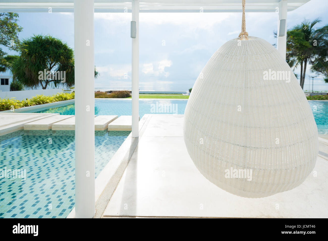 Entspannende weiße Rattan Hängesessel am Pool auf Meerblick für Urlaub, Sommer und Reisen Konzept. Stockfoto