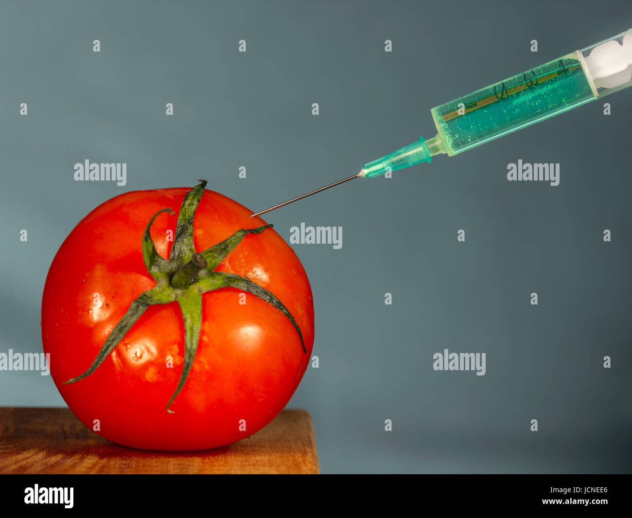 Injektion mit Injektionsnadel eine leuchtende grüne Substanz in eine rote Tomate Stockfoto