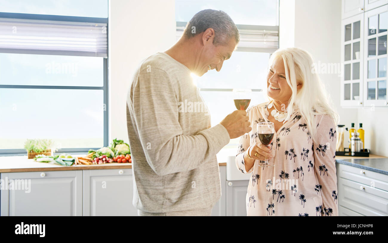 Glückliches Ehepaar im Ruhestand anheben einen Toast Lächeln in jedem anderen Augen, als sie ein Glas Rotwein in einer hohen zentralen weißen Küche genießen Stockfoto