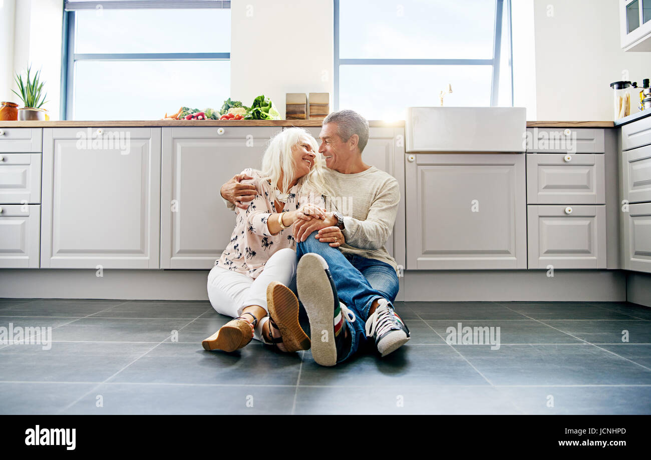 Niedlich älteres paar sahen einander sitzen bequem auf geräumigen dunkle gefliesten Küchenboden Stockfoto