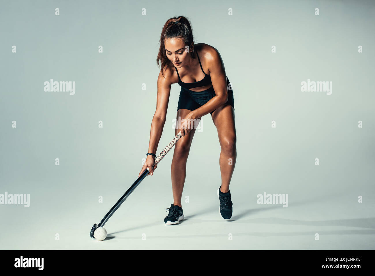 Voller Länge Schuss weibliches Hockey Spieler dribbeln Ball über grau hinterlegt. Hispanische junge Frau im Studio Hockey zu spielen. Stockfoto