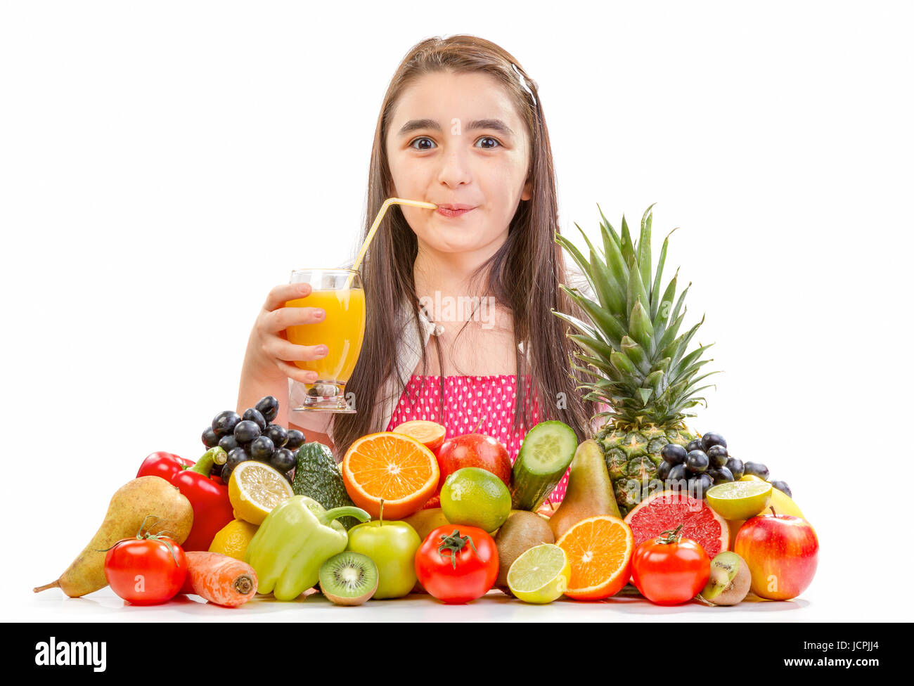 Kleines Mädchen Orangensaft trinken. Kleines Mädchen mit Früchten - fröhliches Mädchen mit Früchten-Sortiment auf dem Tisch. Stockfoto